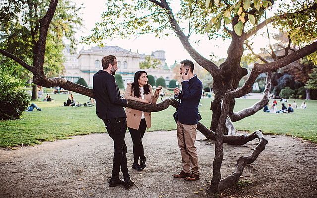 Two men and a woman standing in Stadtpark and speaking