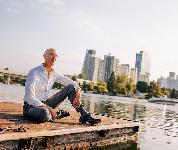 Man in white shirt sitting casually at pier and looking at the Donau