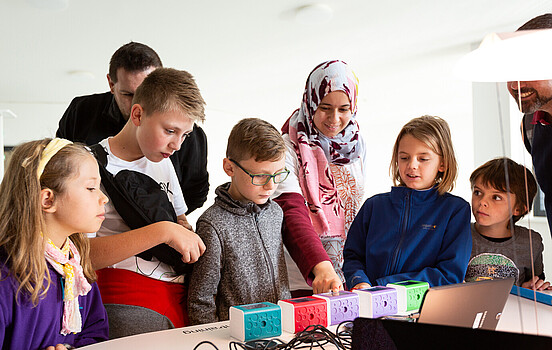 A group of schoolchildren looking at a technological object with their female teacher